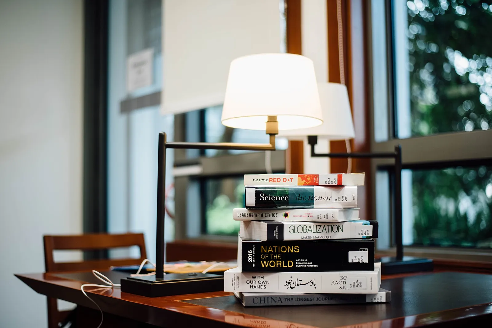A stack of books on a desk beside two reading lamps